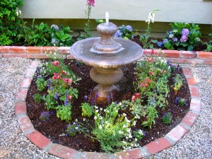 Recycled brick used as garden edging in English tea garden with cast stone fountain and perennials
